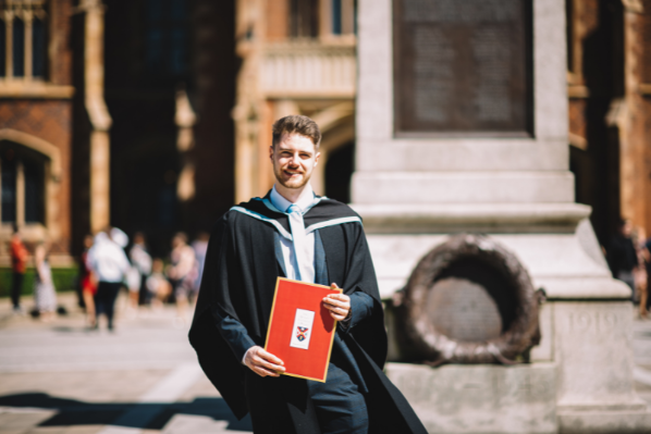 Male student standing outside Queen's University main door in graduation gown