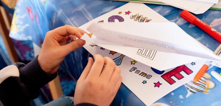 child making paper aeroplane from colouring book page