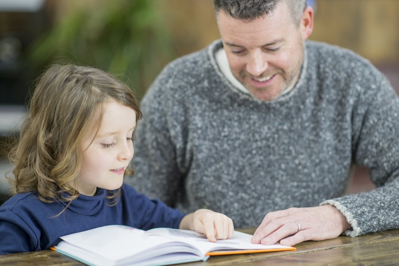 father and daughter reading a book at the table