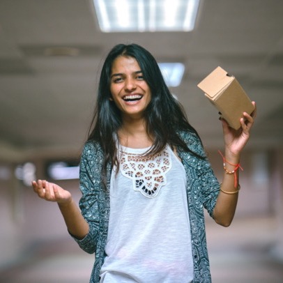 A girl holds a cardboard headset while smiling