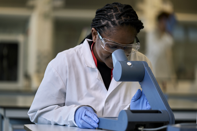 Researcher wearing lab coat looking through microscope